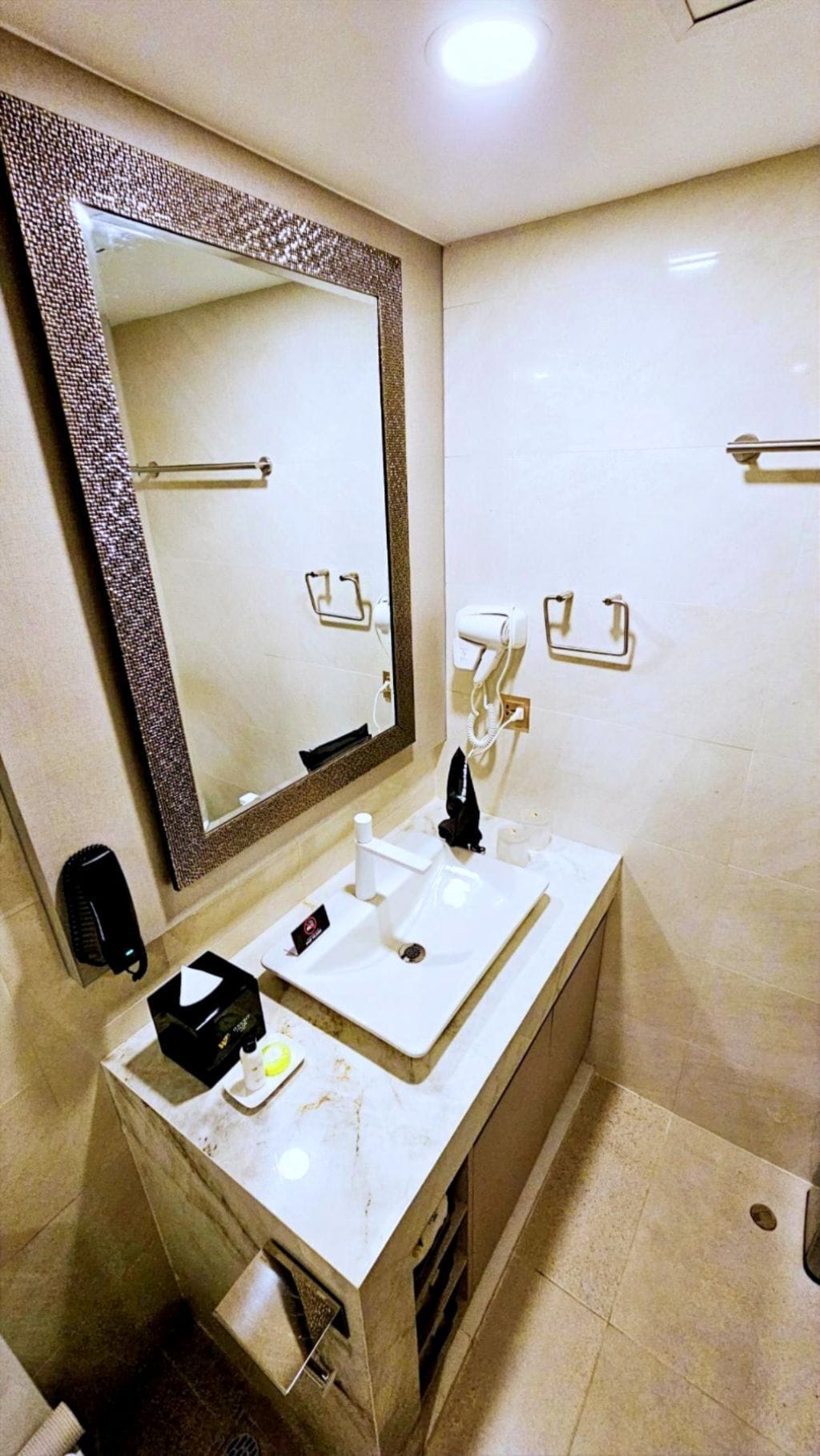 Un baño con un espejo grande, un lavamanos, un secador de pelo y un perchero para toallas.
