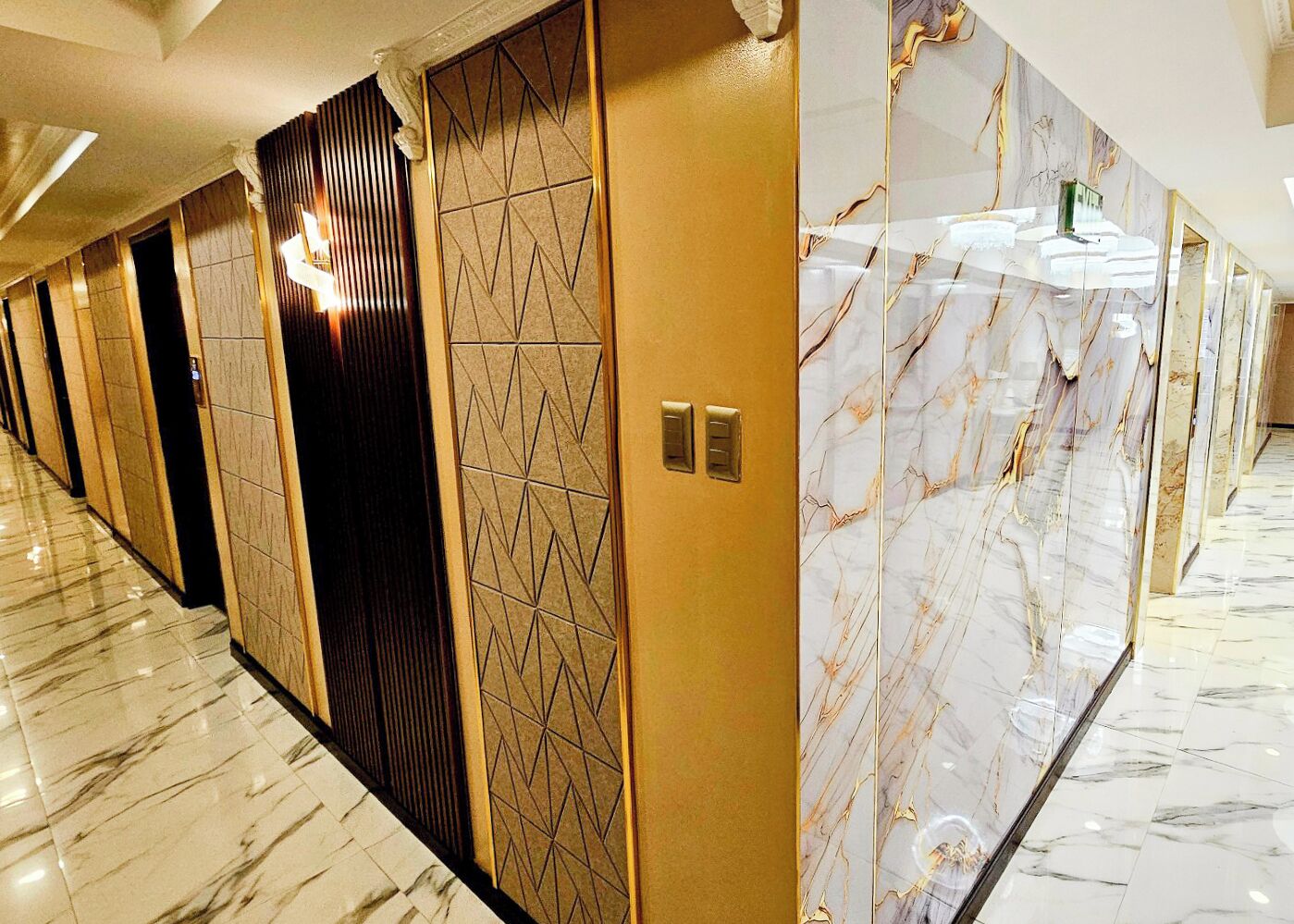 A hotel corridor with marble flooring, a modern elevator, and a wall with geometric patterns.