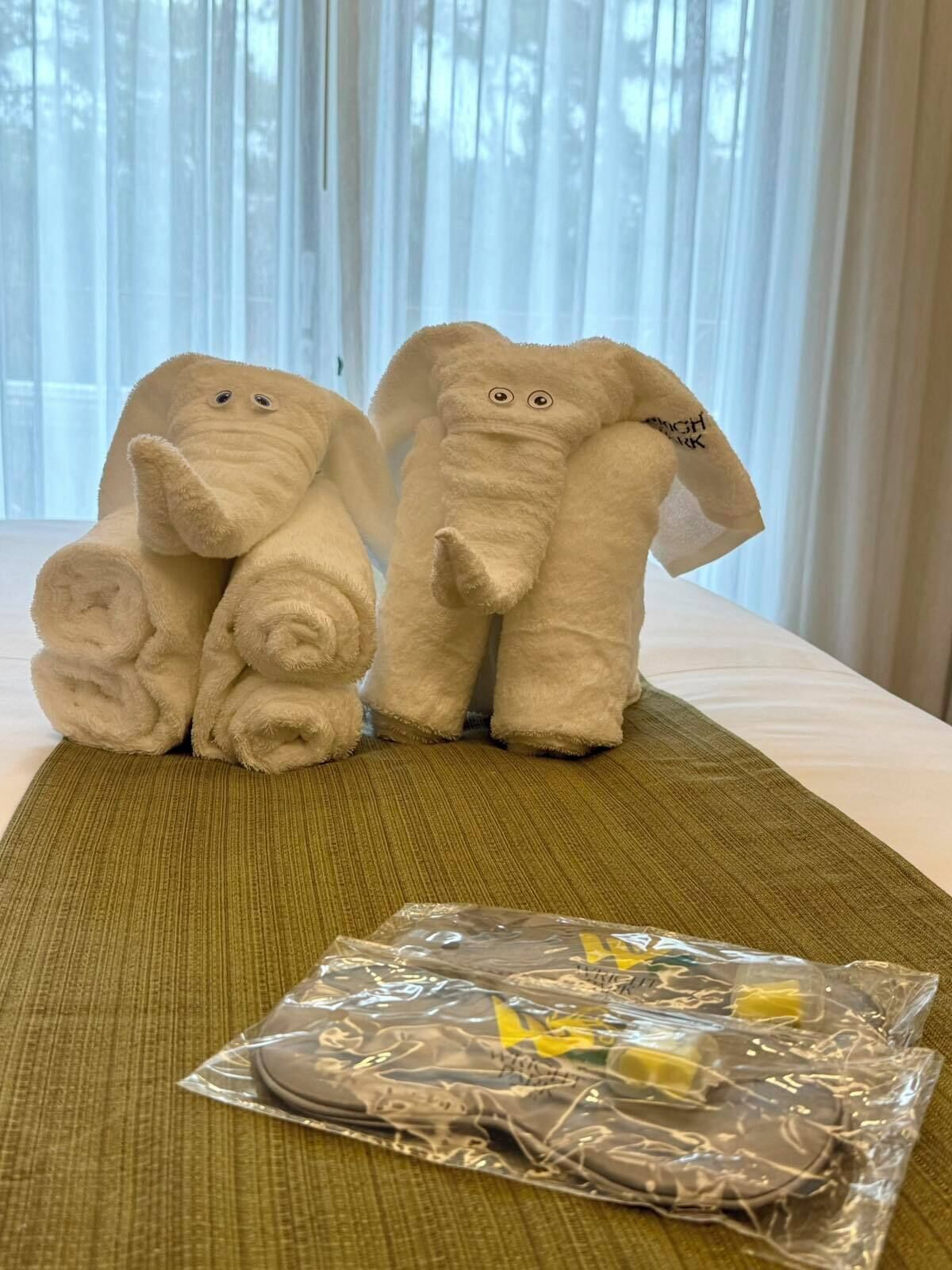 Two plush elephant toys on a bed with a green mat. A plastic bag with items is on the bed.
