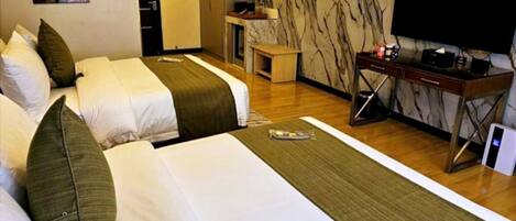A hotel room with two beds, a desk, a television, and a ceiling fan.