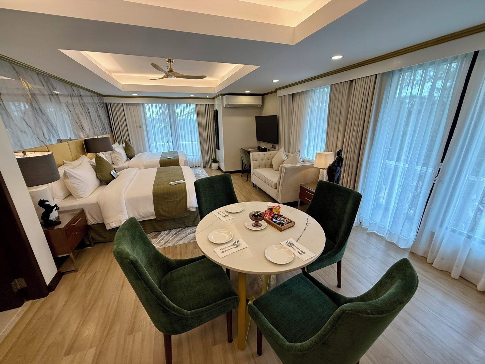 Una habitación de hotel con dos camas, una mesa de comedor con sillas, un sofá y un ventilador de techo.
