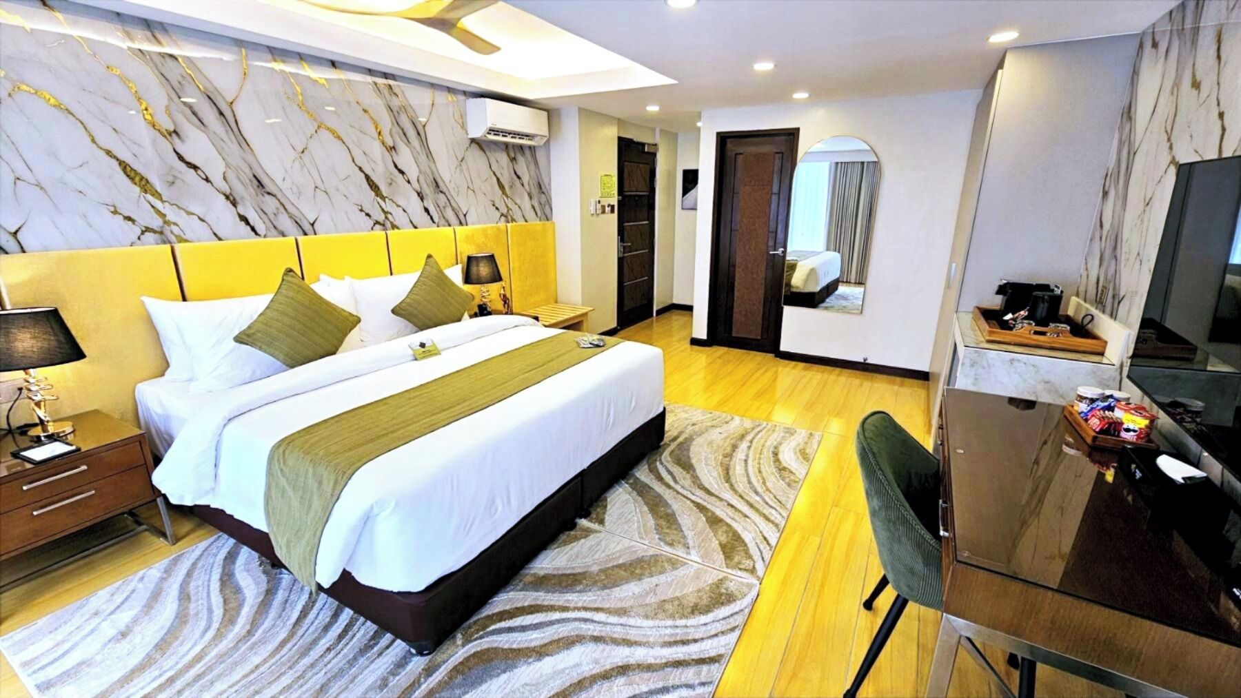 A modern hotel room with a large bed, a desk with a chair, a TV, and a bathroom visible through an open door.