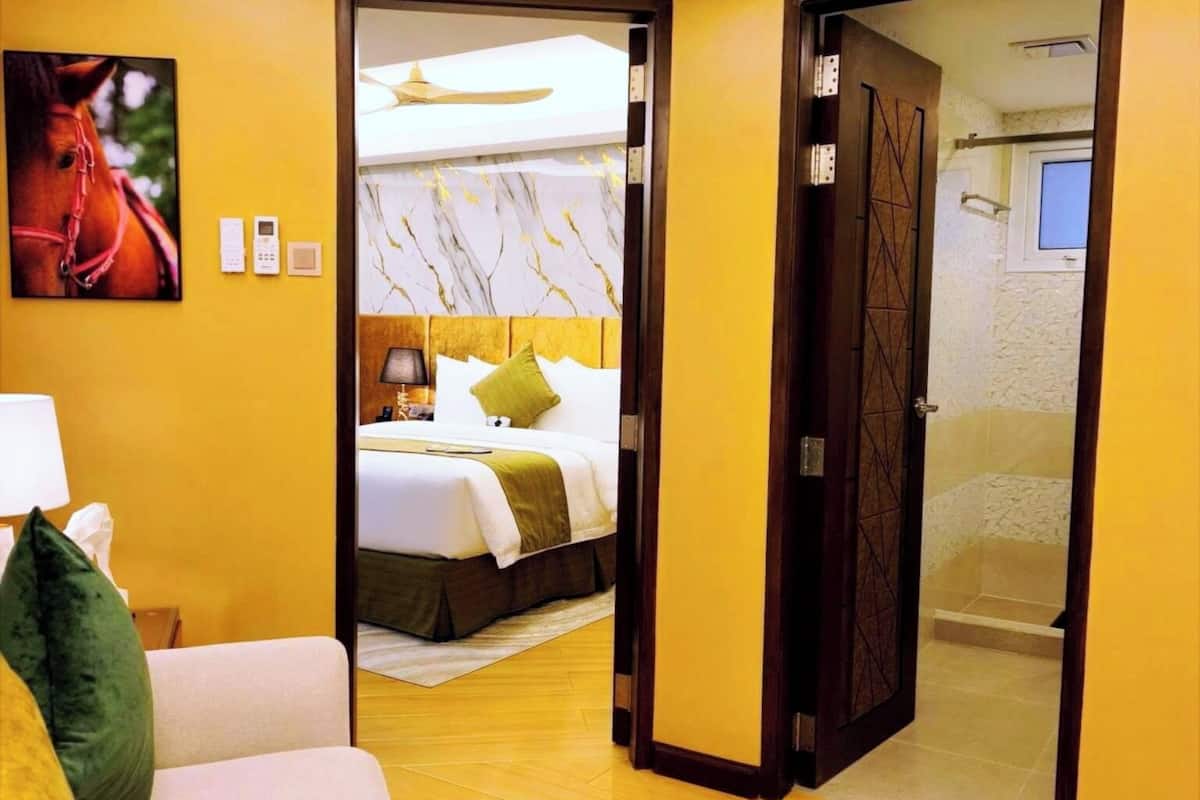 Ein Hotelzimmer mit Bett, Sofa, Hocker, einem Gemälde von einem Pferd und einem durchgegangenen Tür erkennbaren Badezimmer.