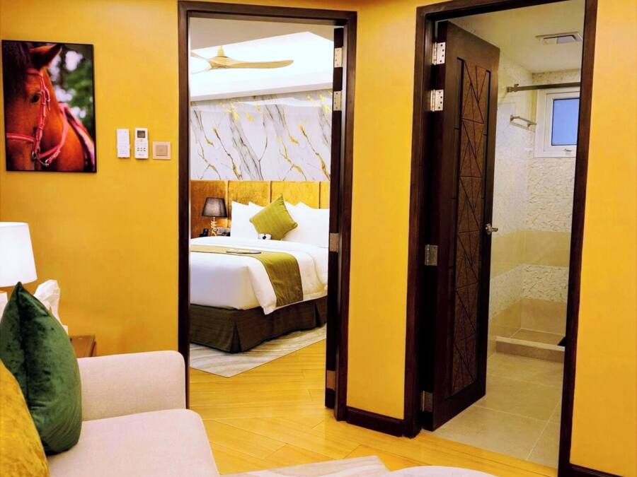 Habitación de hotel con cama, sofá, reposapiés, un cuadro de un caballo y un baño visible a través de una puerta abierta.