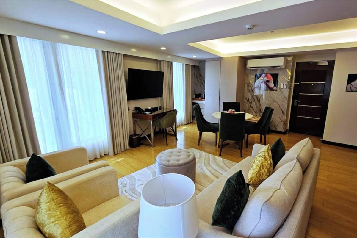Ein modernes Wohnzimmer mit einer Sofagarnitur, einem Couchtisch und einem Fernseher. Es gibt einen Essbereich mit Tisch und Stühlen sowie eine Küchenzeile mit einer Mikrowelle und einem Kühlschrank.