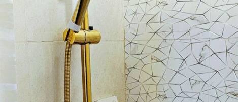 A shower with a gold fixture, a wall-mounted shelf with toiletries, and a geometric tile pattern.