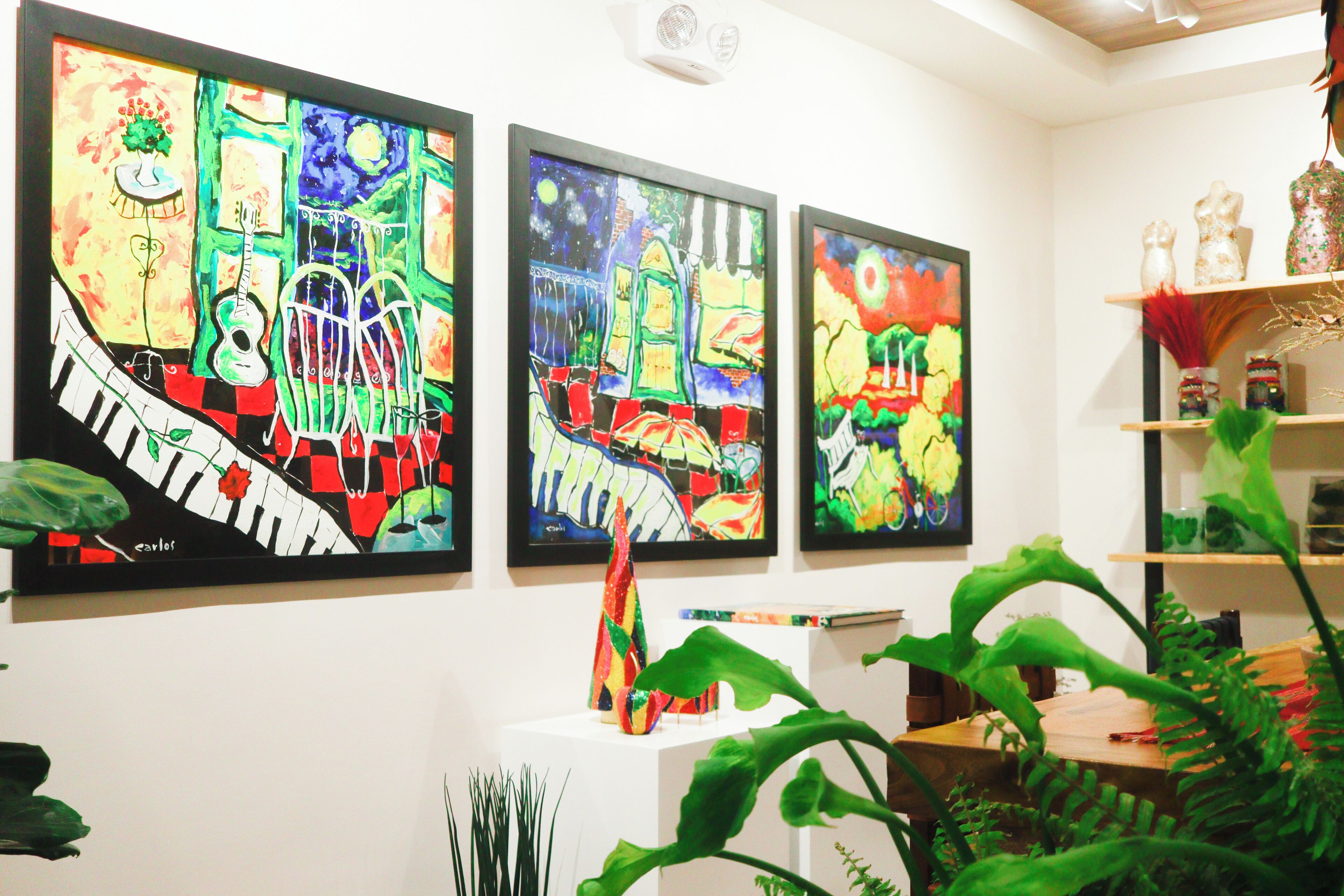 A room with three large paintings on the wall, a white pedestal with a vase, and a wooden shelf with decorative items.
