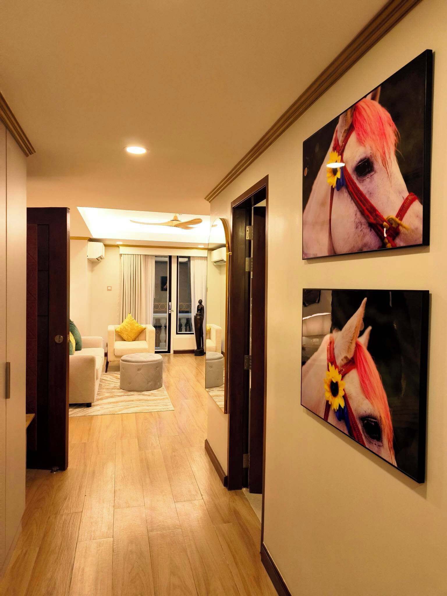 A hallway with a wooden floor, a sofa, a coffee table, and two paintings of horses.