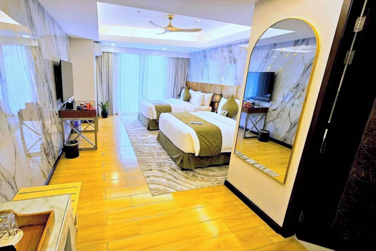 Ein Hotelzimmer mit einem großen Bett, einem Schreibtisch, einem Sessel, einem Spiegel und einem Deckenventilator.