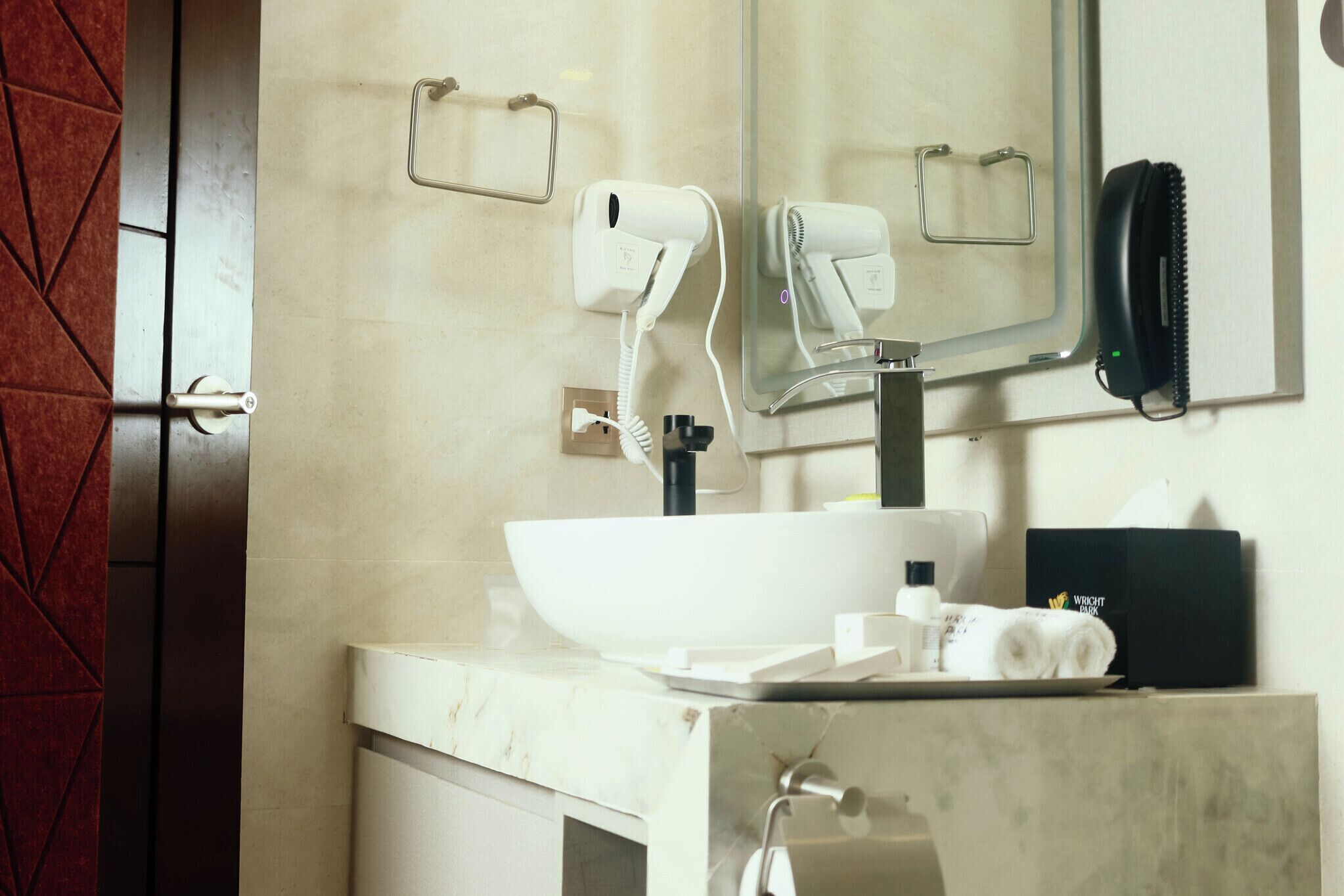 A bathroom with a white sink, a mirror, a hairdryer, and a telephone.