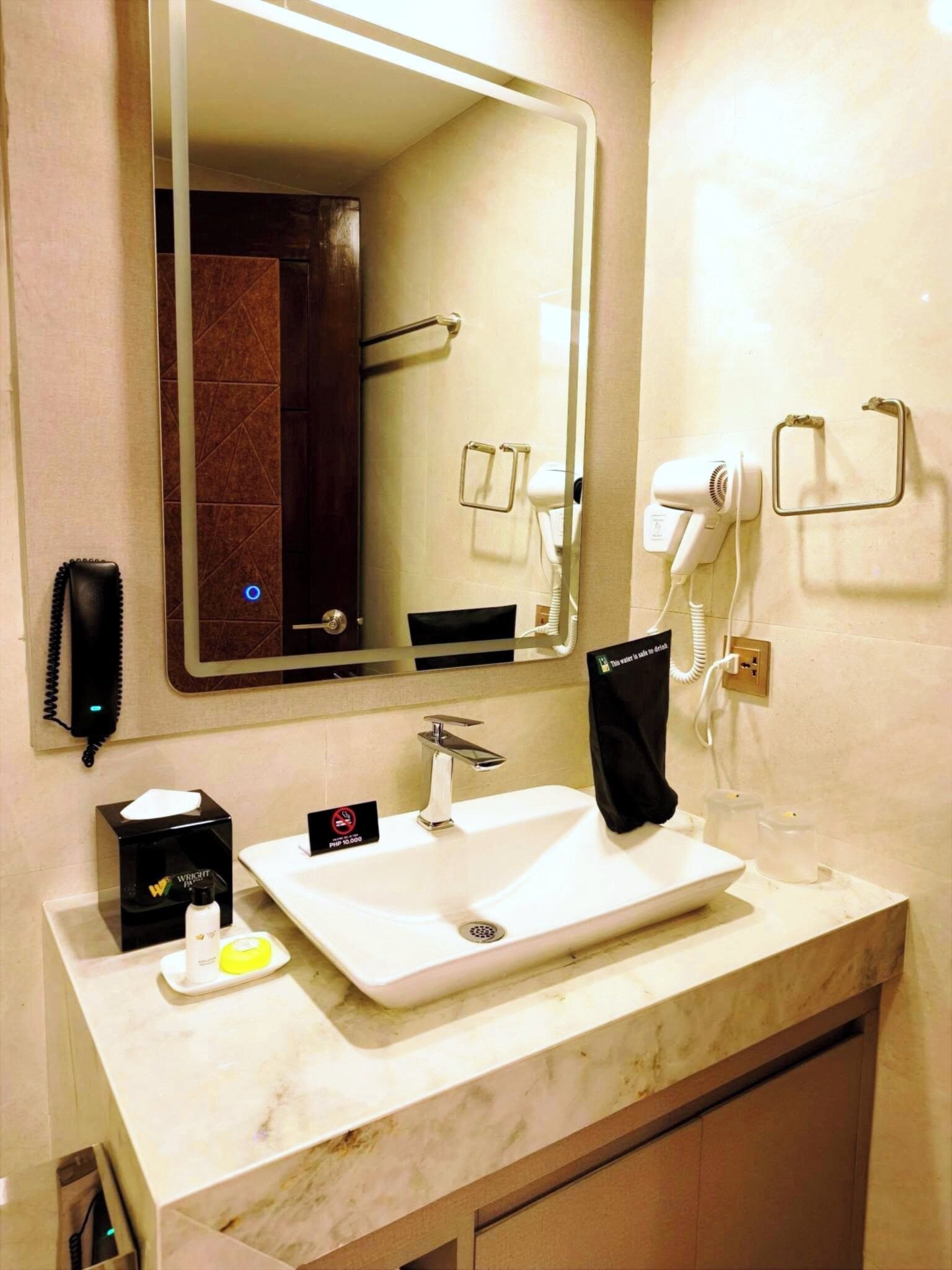 A hotel bathroom with a white sink, a mirror, a hairdryer, and a towel rack.