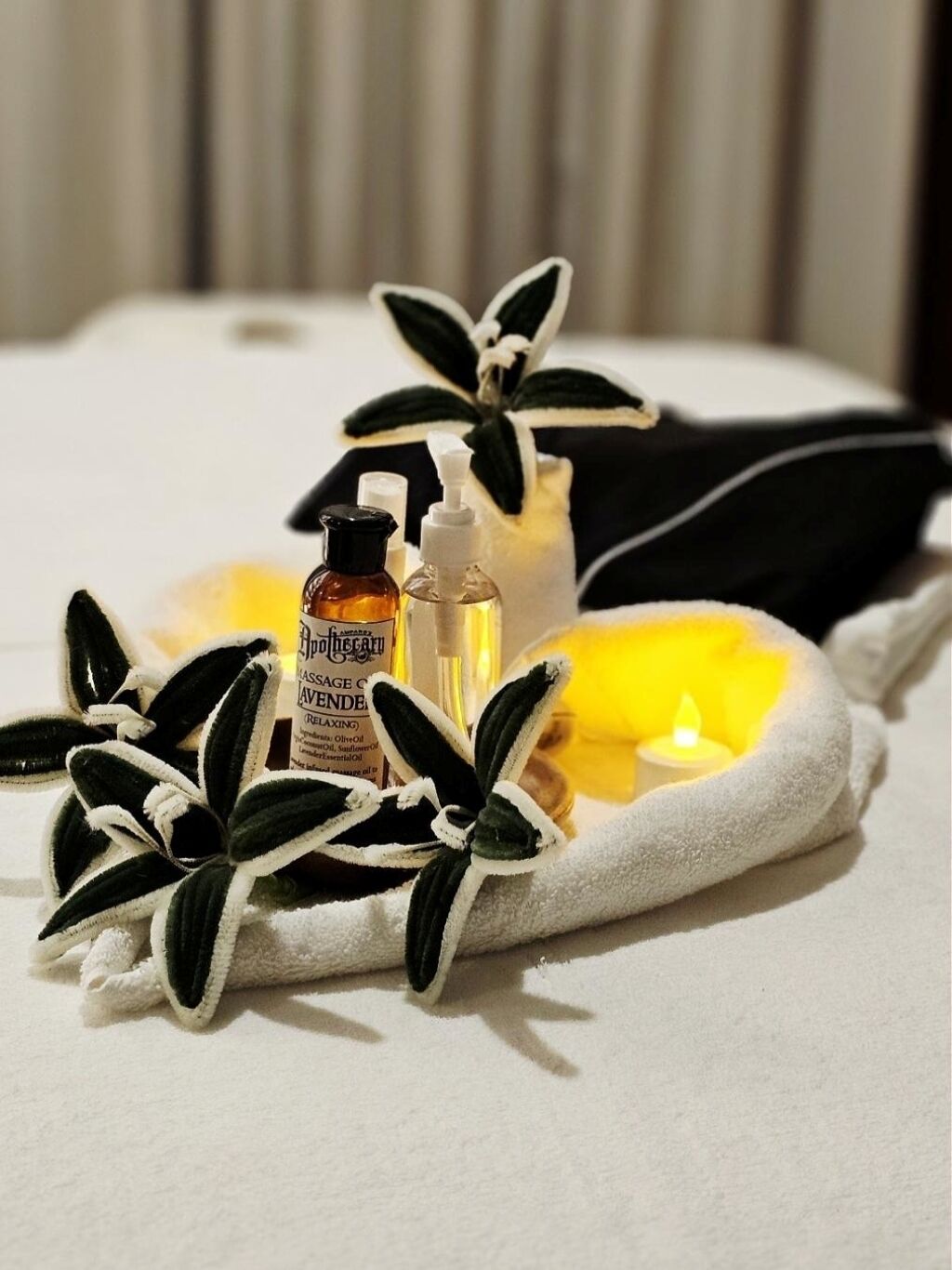 A spa setting with a massage table, black and white decorative plants, and bottles of essential oils.