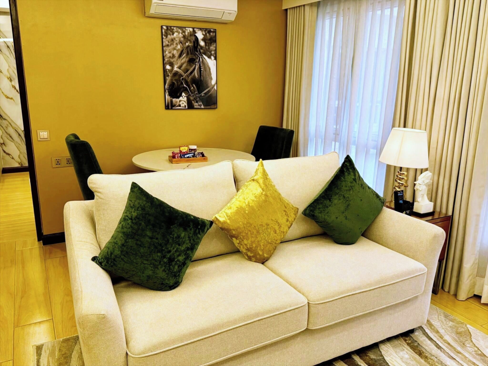 A modern living room with a beige sofa, green and gold cushions, a round coffee table, and a painting on the wall.