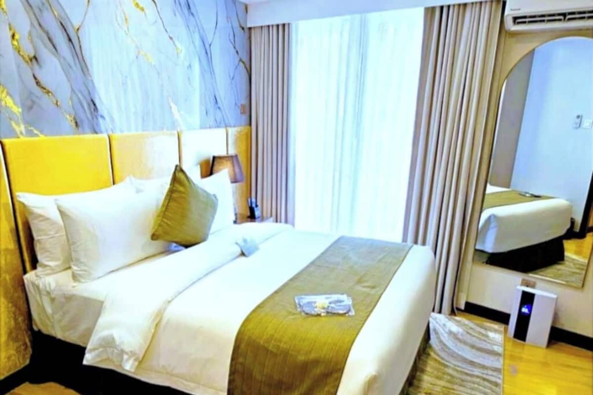 Ein Hotelzimmer mit einem großen Bett, einem Kopfteil, einem Nachttisch, einem Spiegel und einem Fenster mit Vorhängen.