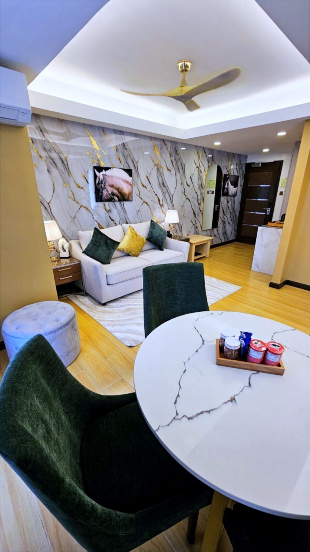 A modern living room with a white sofa, green and yellow cushions, a round marble table, and a ceiling fan.