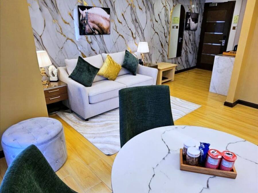 Un saló modern amb un sofà blanc, coixins verds i grocs, una taula rodona de marbre i un ventilador de sostre.