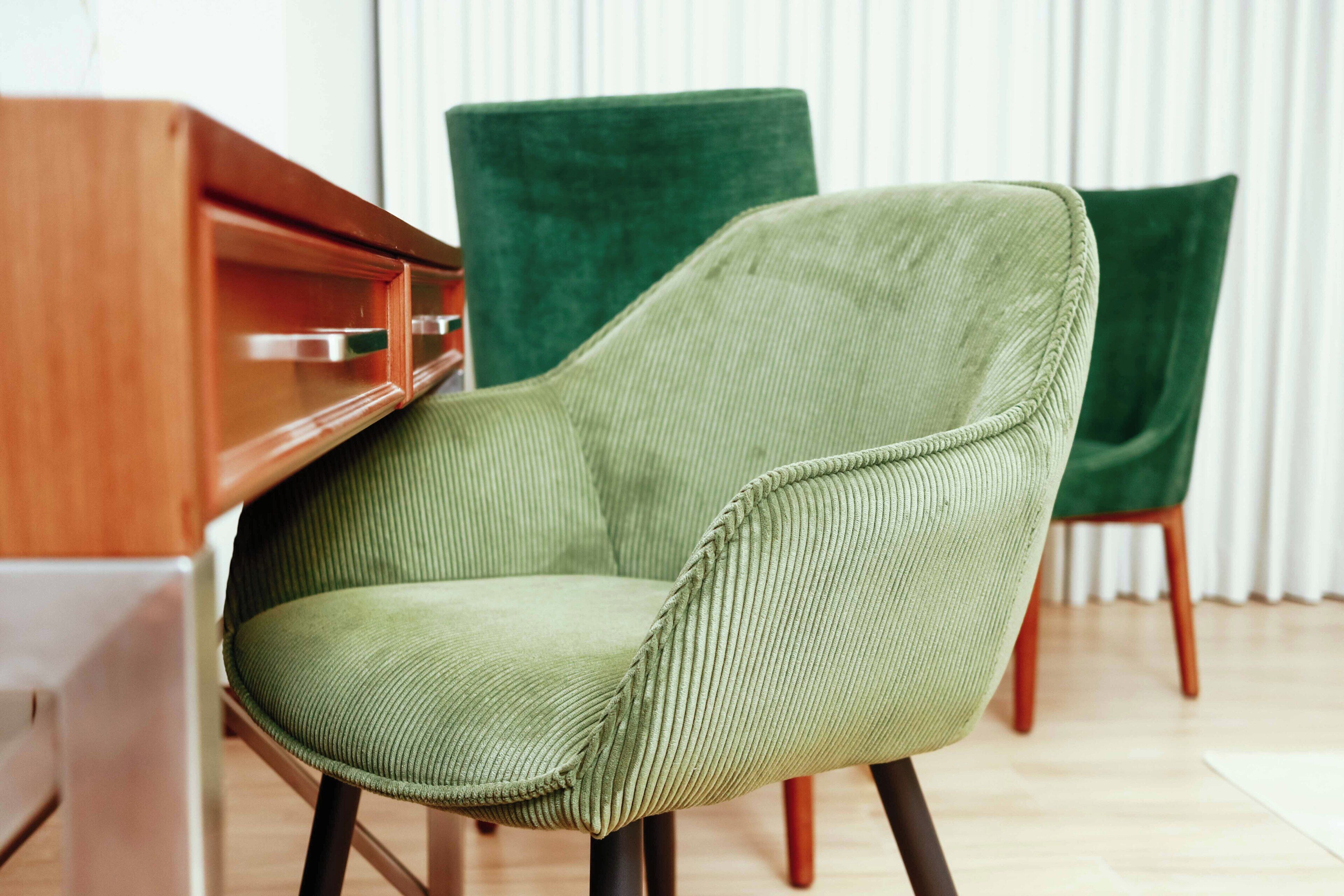 A green upholstered chair with a ribbed texture, positioned in front of a wooden desk and a green upholstered chair.