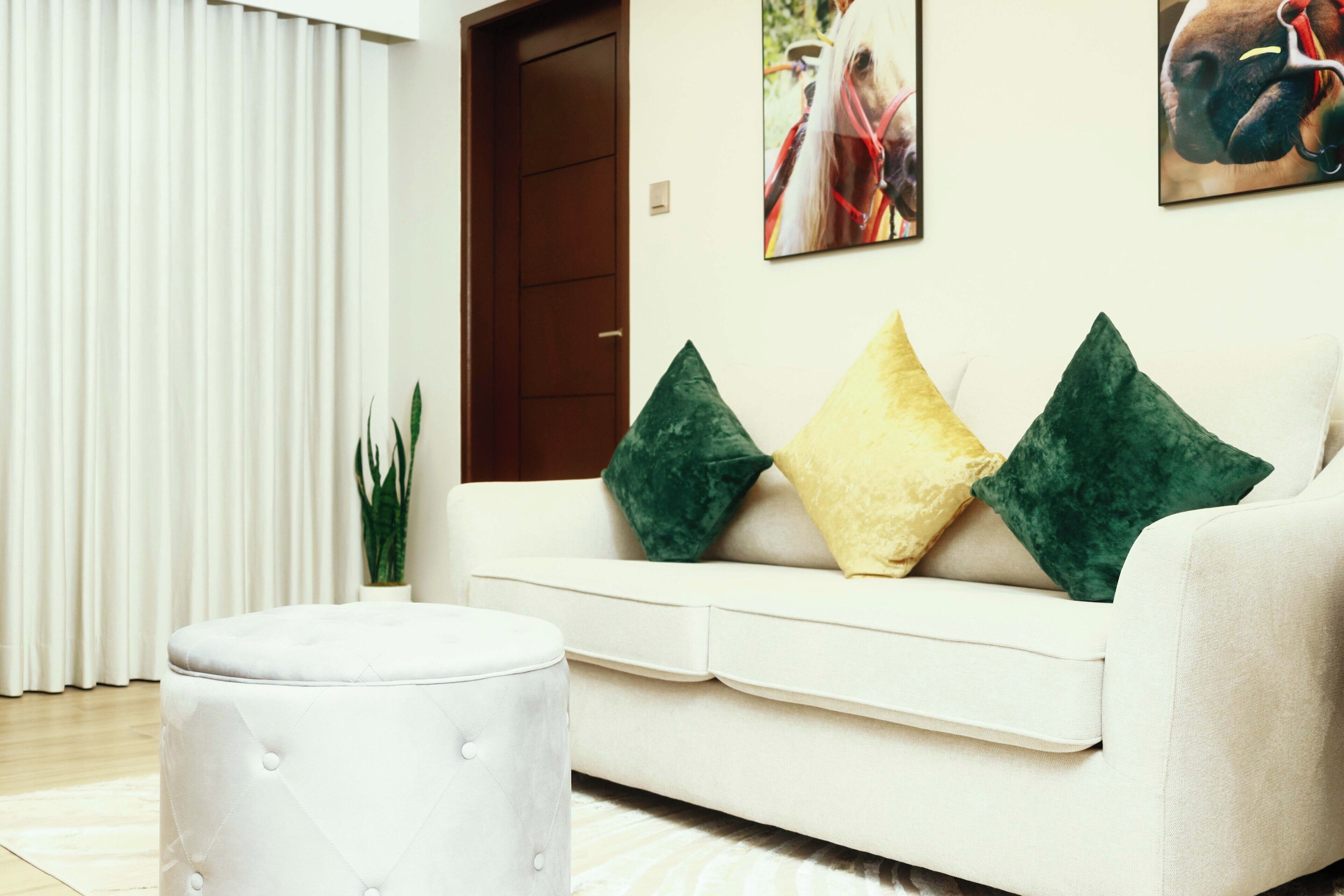 A living room with a white sofa, green and yellow cushions, and a white ottoman.