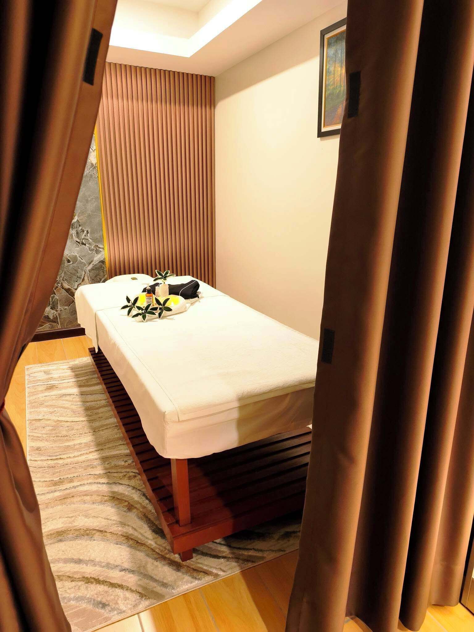 A small, cozy room with a bed, a wooden floor, a striped rug, and a window with blinds.