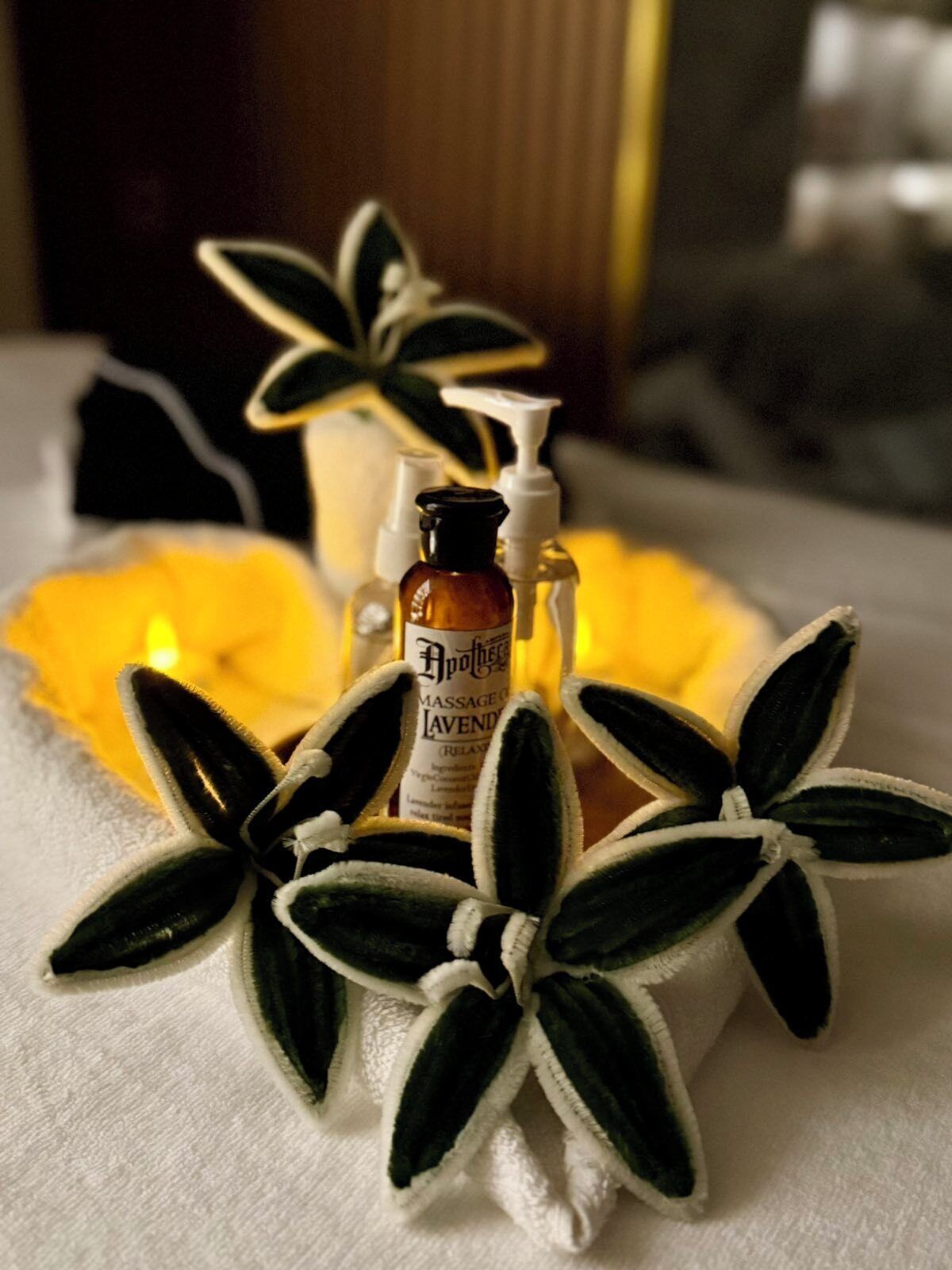 Una botella de aceite de masaje etiquetada 'Apothecary Lavender' y una botella blanca dosificadora sobre una toalla blanca con decoraciones en forma de estrella.