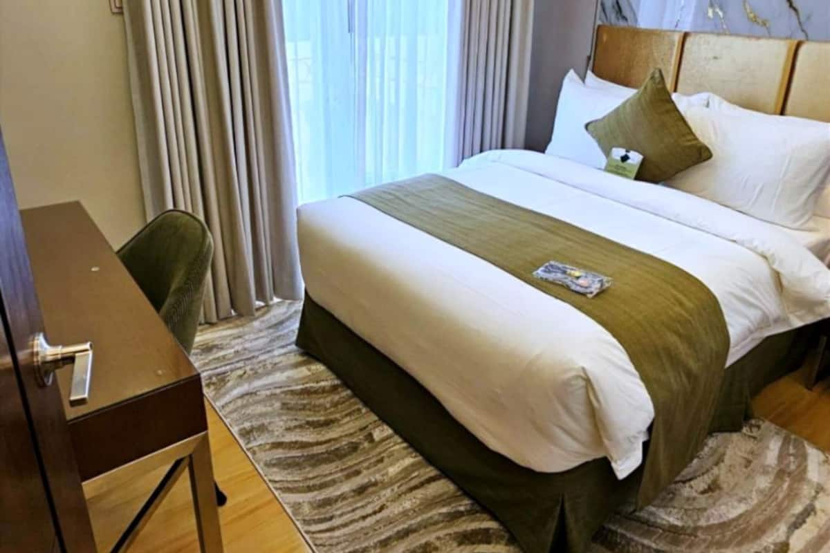 Ein Hotelzimmer mit einem großen Bett, einem Schreibtisch und Blick ins Freie durch das Fenster.