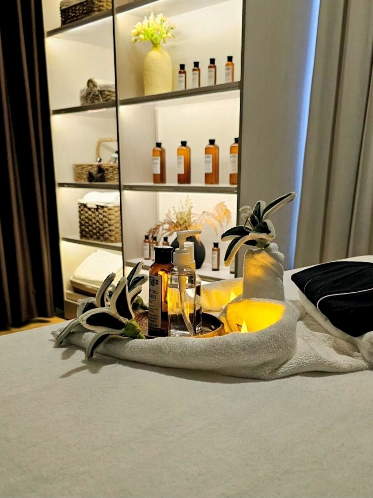 A neatly arranged tray with toiletries and a candle on a table, with a shelf of bottles and decorative items in the background.