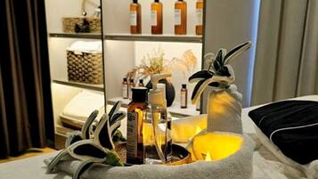 A neatly arranged tray with toiletries and a candle on a table, with a shelf of bottles and decorative items in the background.