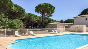 Ein Schwimmbecken mit Liegestühlen, einem umzäunten Bereich und einem Gebäude mit einem Ziegeldach.
