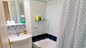 Ein Badezimmer mit weißem Waschbecken, einem Spiegel, einer Ablage mit Toilettenartikeln, einer Badewanne und einer Duschvorhang.