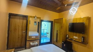 A hotel room with a bed, a TV mounted on the wall, a wooden wardrobe, and a small table with a kettle.