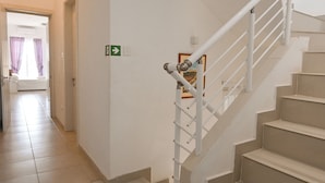 A staircase with a handrail, a door with a green directional sign, and a framed picture on the wall. - Il-qastna Holiday House-zejtun (Zejtun)