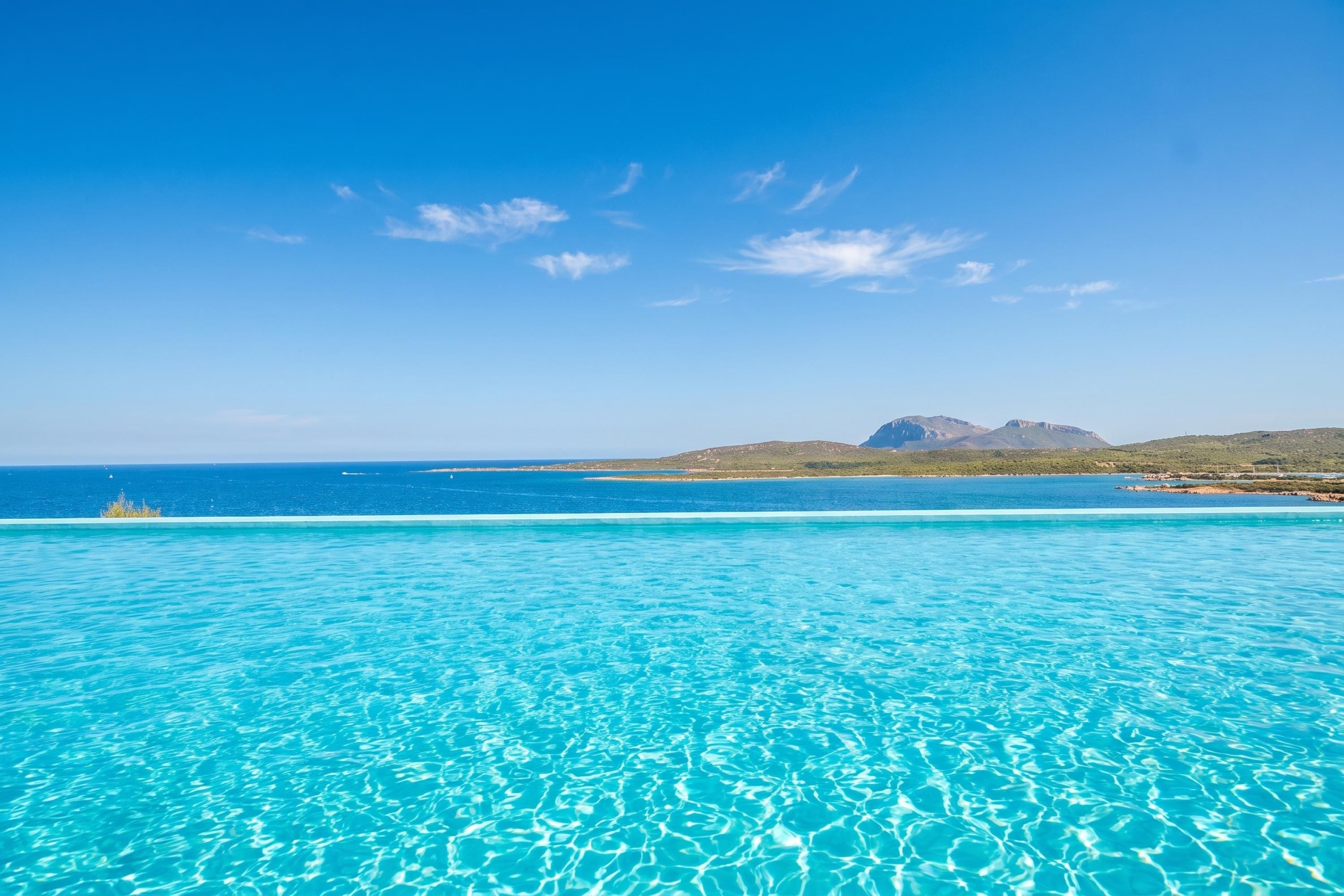 A clear blue pool with a view of the ocean and distant mountains.