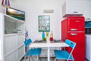 A dining area with a white table, blue chairs, a red refrigerator, and a wall-mounted poster. - Vacanze Da Giuly With Shared Pool (Olbia)