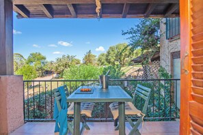 A balcony with a table and chairs, a metal pot, and a view of trees and a building. - Vacanze Da Giuly With Shared Pool (Olbia)