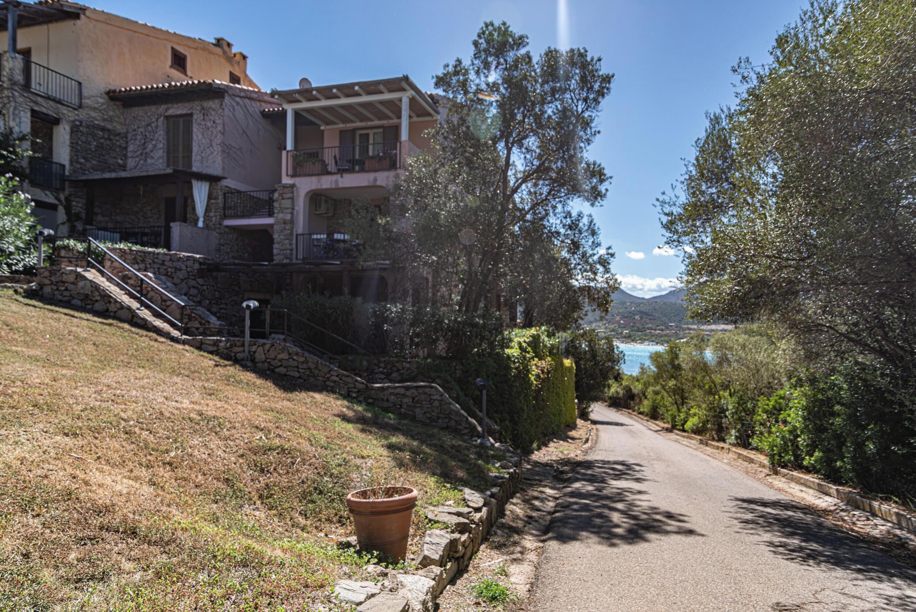 Uma estrada costeira com degraus de pedra que levam a um edifício com varandas com vista para o mar.