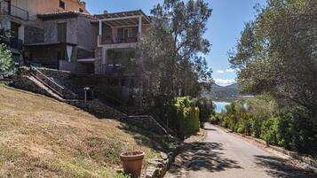 Uma estrada costeira com degraus de pedra que levam a um edifício com varandas com vista para o mar.