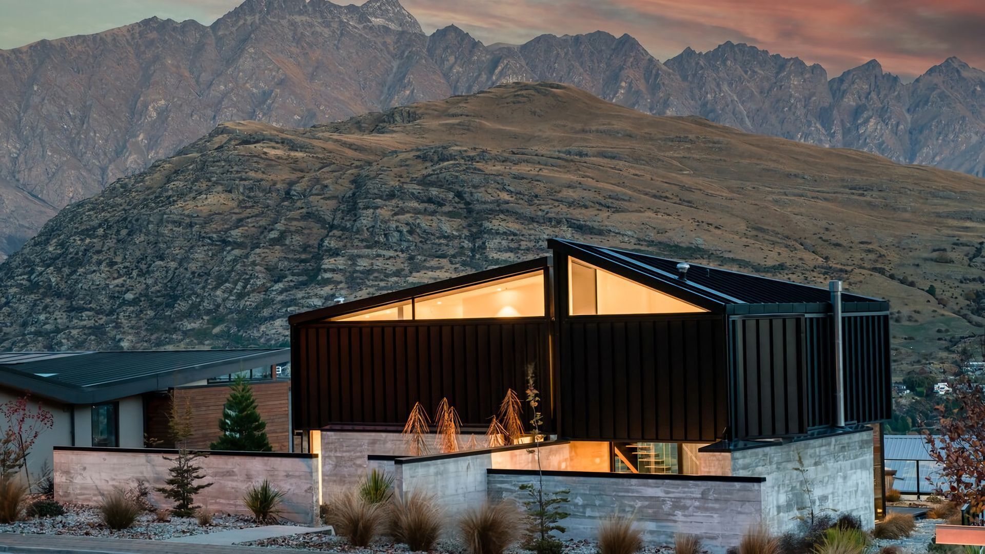 A modern house with a large glass window, surrounded by a landscaped garden with native plants.