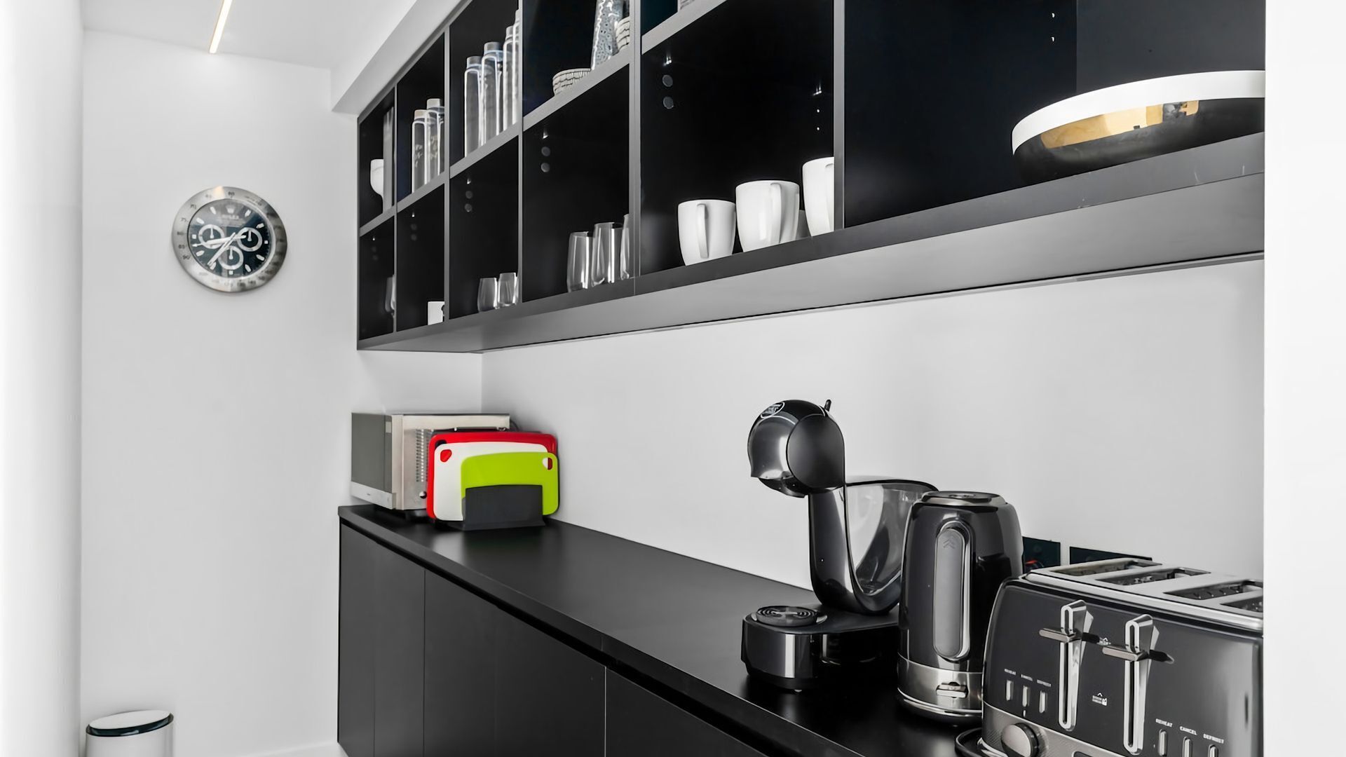 Una cocina moderna con armarios negros, una cafetera, un tostador y un reloj en la pared.