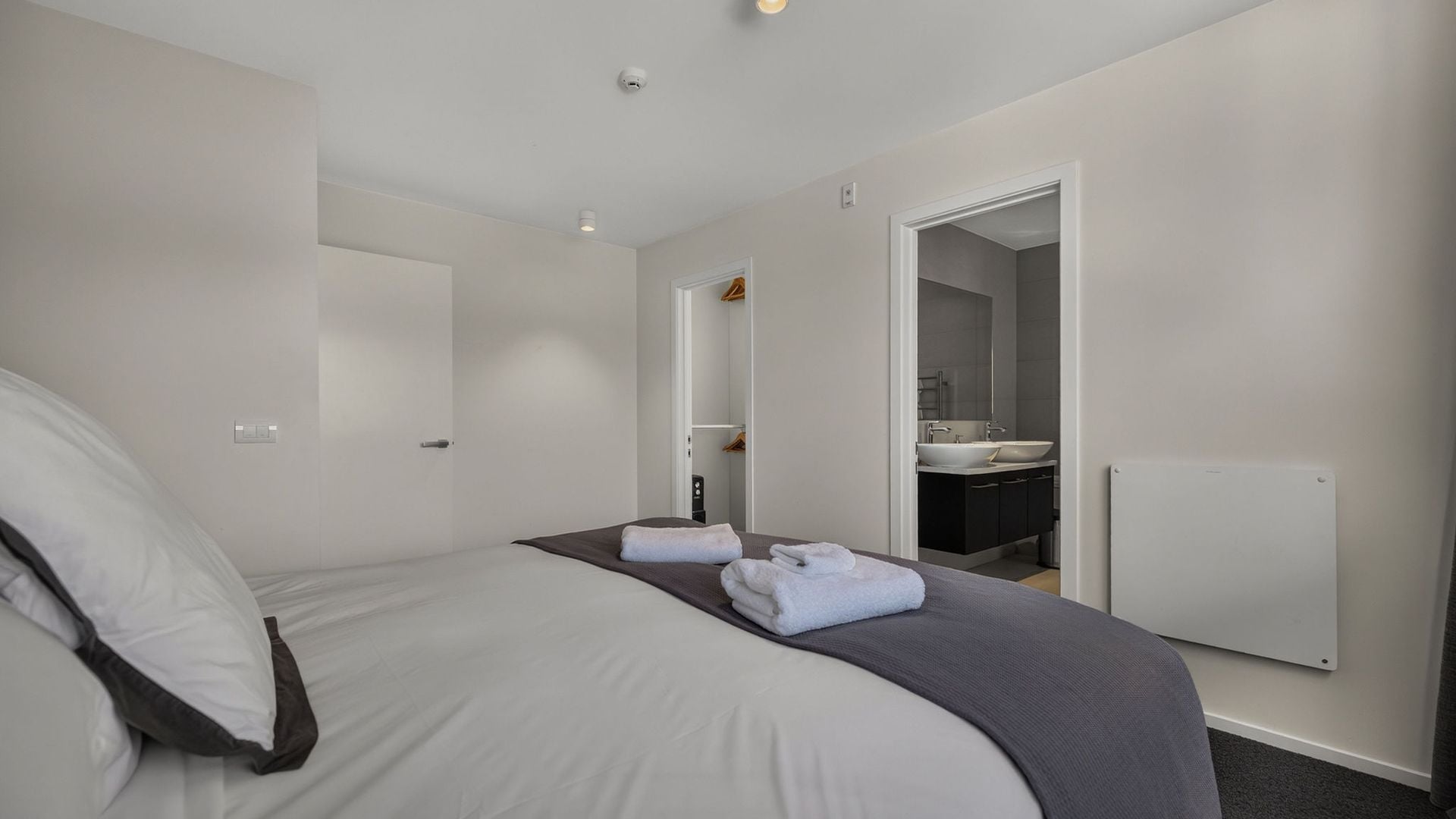 Une chambre d’hôtel comprenant un lit, une salle de bain avec un lavabo et un miroir, et une porte donnant sur une autre pièce.