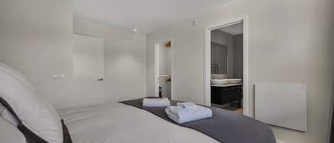 Une chambre d’hôtel comprenant un lit, une salle de bain avec un lavabo et un miroir, et une porte donnant sur une autre pièce.