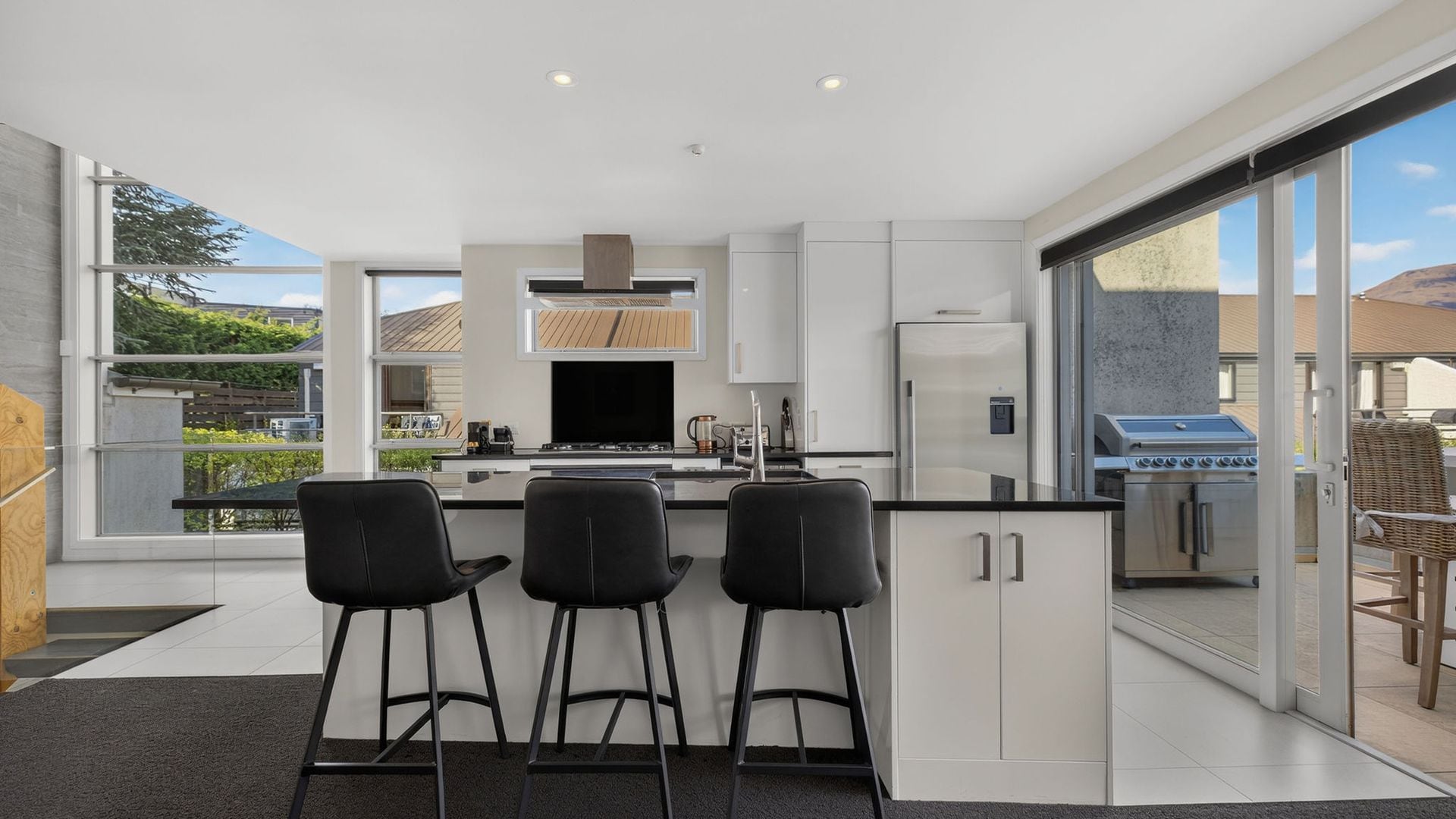 A modern kitchen with a central island, bar stools, and a view of the outdoors.