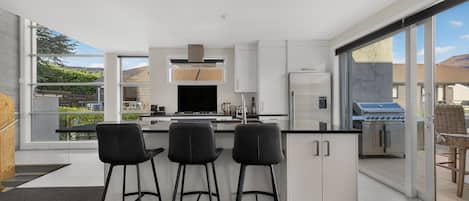 A modern kitchen with a central island, bar stools, and a view of the outdoors.