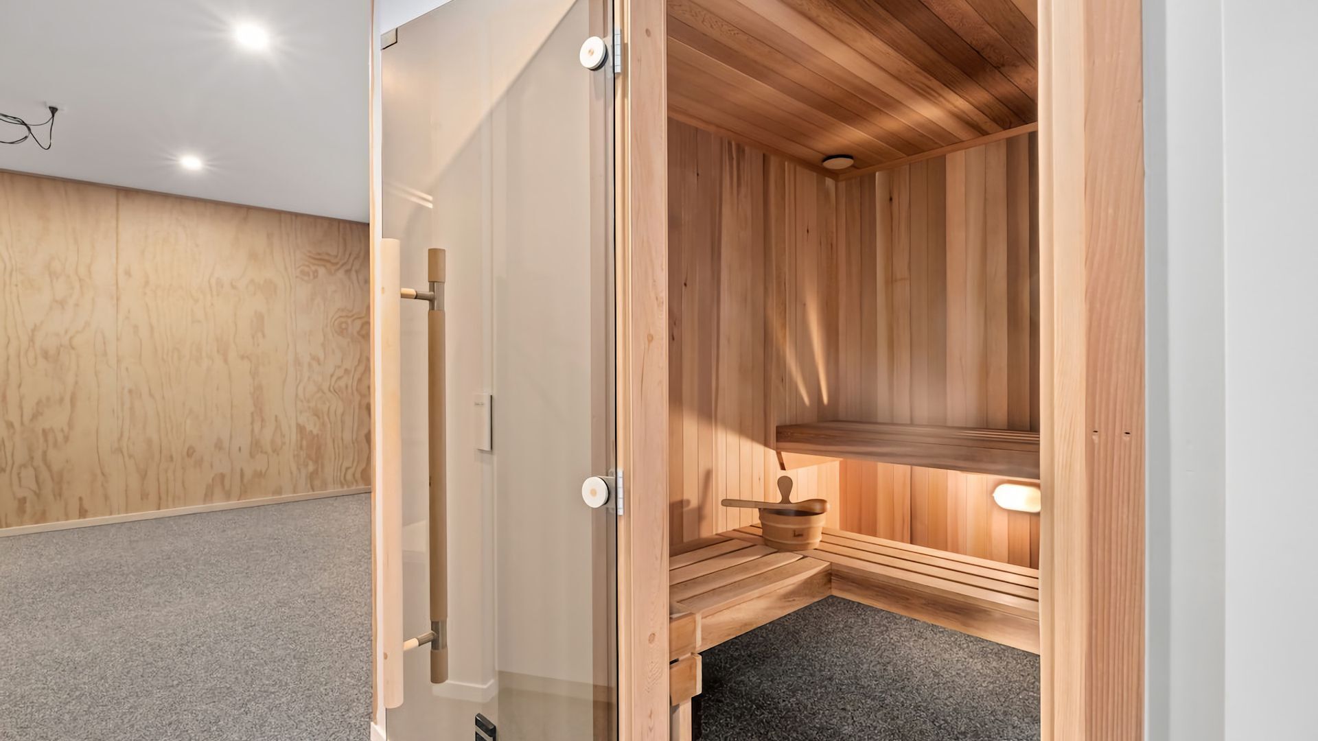 Eine Holzsauna mit einer Bank, einem kleinen Tisch, einer Tür und einer Lampe.