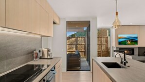 A modern kitchen with a built-in oven, a coffee machine, and a large window overlooking a mountainous landscape. - Central Queenstown Villa Spa (Queenstown)