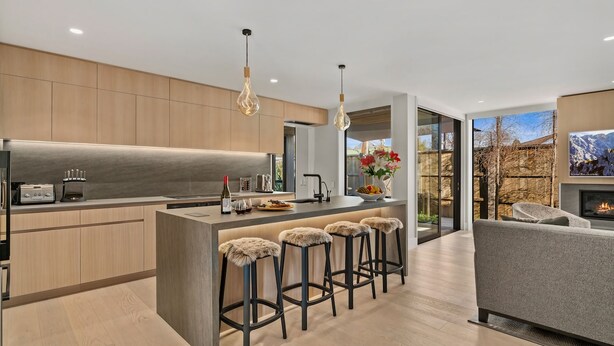 A modern kitchen with a central island, bar stools, and a dining area with a sofa. - Central Queenstown Villa Spa (Queenstown)