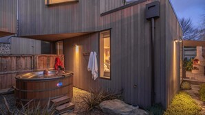 A modern house with a hot tub, a stone fireplace, and a wooden deck. - Central Queenstown Villa Spa (Queenstown)