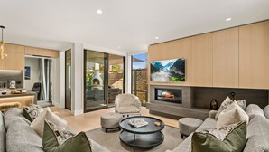 A modern living room with a fireplace, comfortable seating, and a kitchen area visible through glass doors. - Central Queenstown Villa Spa (Queenstown)