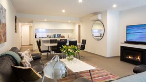 A modern living room with a sofa, coffee table, and a fireplace. There is a dining area with chairs and a kitchen in the background. - Apartment G3 3BR Near Queenstown Centre (Queenstown)