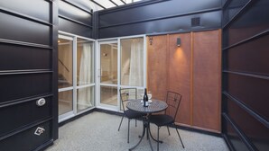 Ein Eckzimmer mit Glastür, einem kleinen runden Tisch mit Stühlen und einer Wand aus Holzpaneelen.