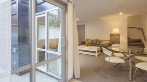 Ein modernes Wohnzimmer mit Glastür zu einem Balkon, einem grünen Sofa, einem Couchtisch und einem Essbereich mit Stühlen.
